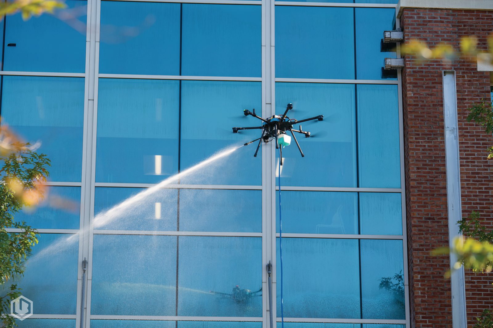 A drone soft-washing the glass facade of a commercial building