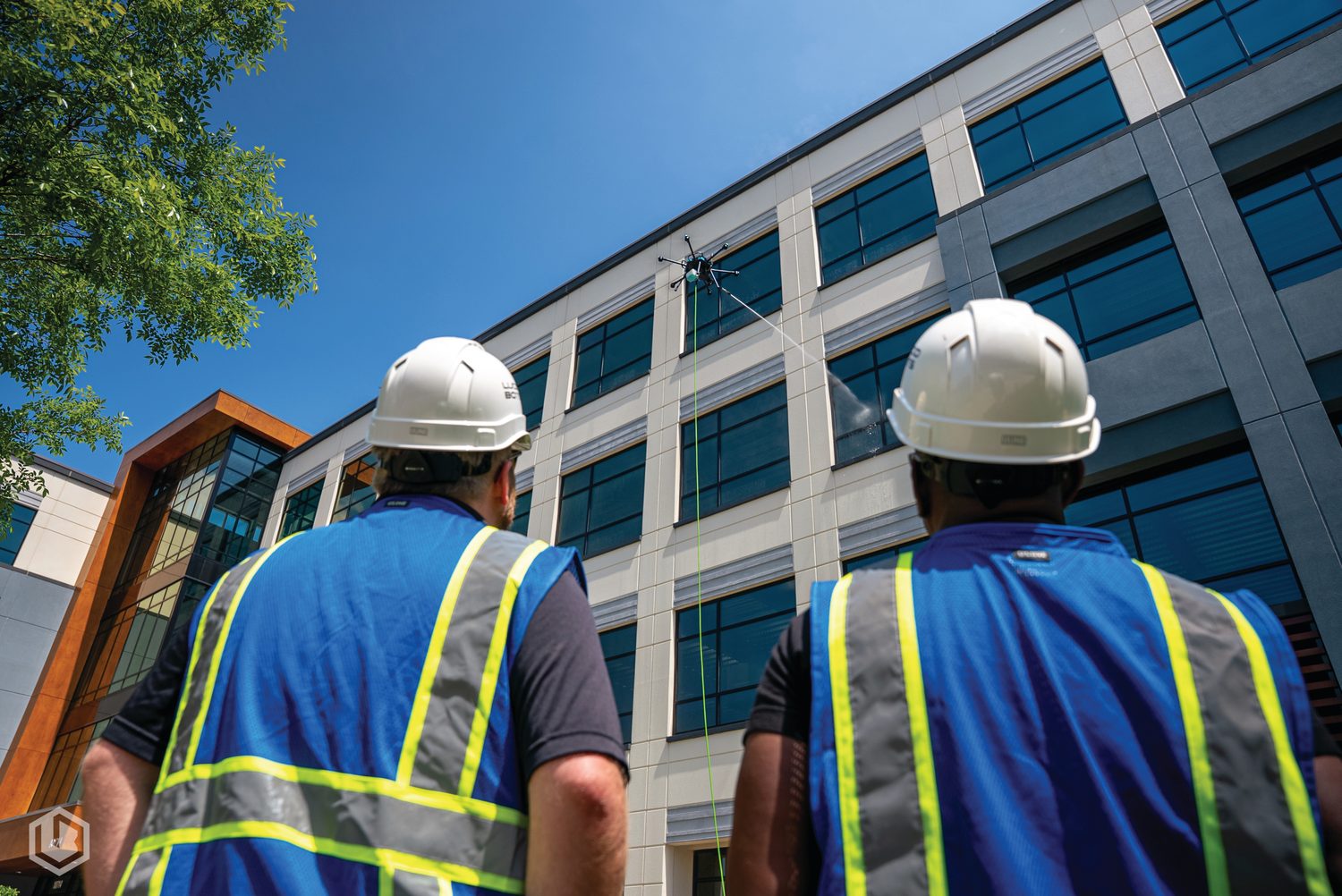 A drone soft-washing a commercial building while the ground crew watches from below